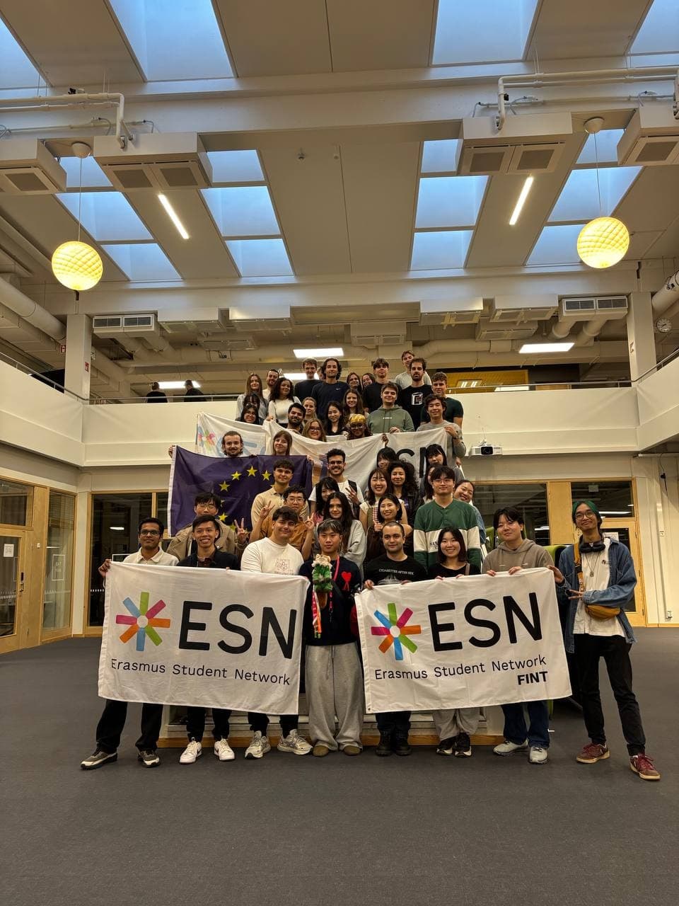 Large group of students holding ESN and EU flags on campus stairs